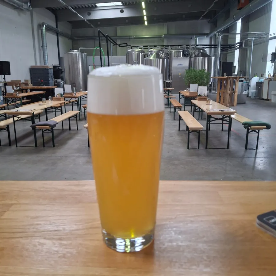 Frisch gezapftes Hawara auf dem Tisch in der Braustube, im Hintergrund das Sudhaus und die Biertische